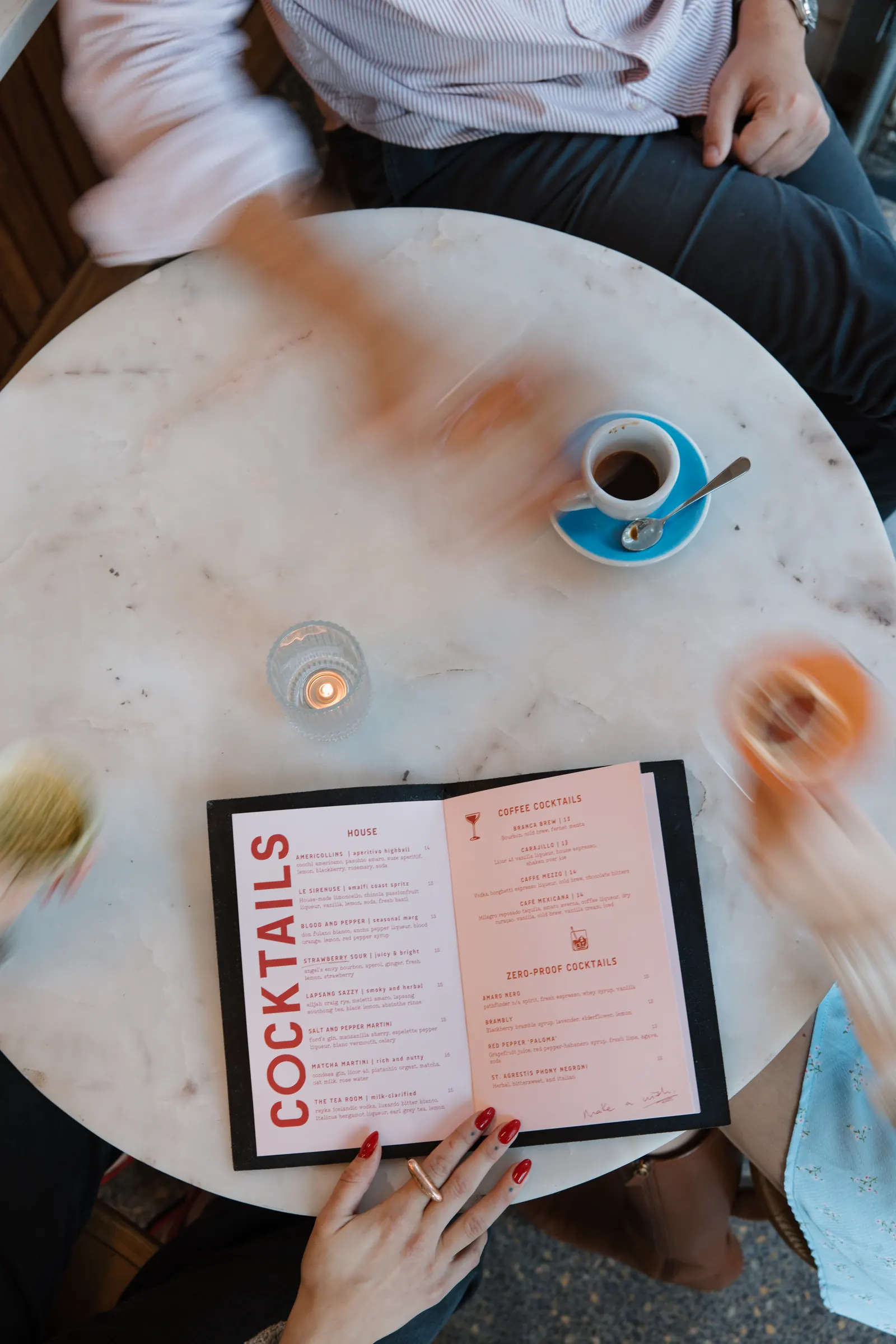 Overhead of a marble table with cocktails, coffee and a menu, hands blurred by slow shutter at Intermezzo