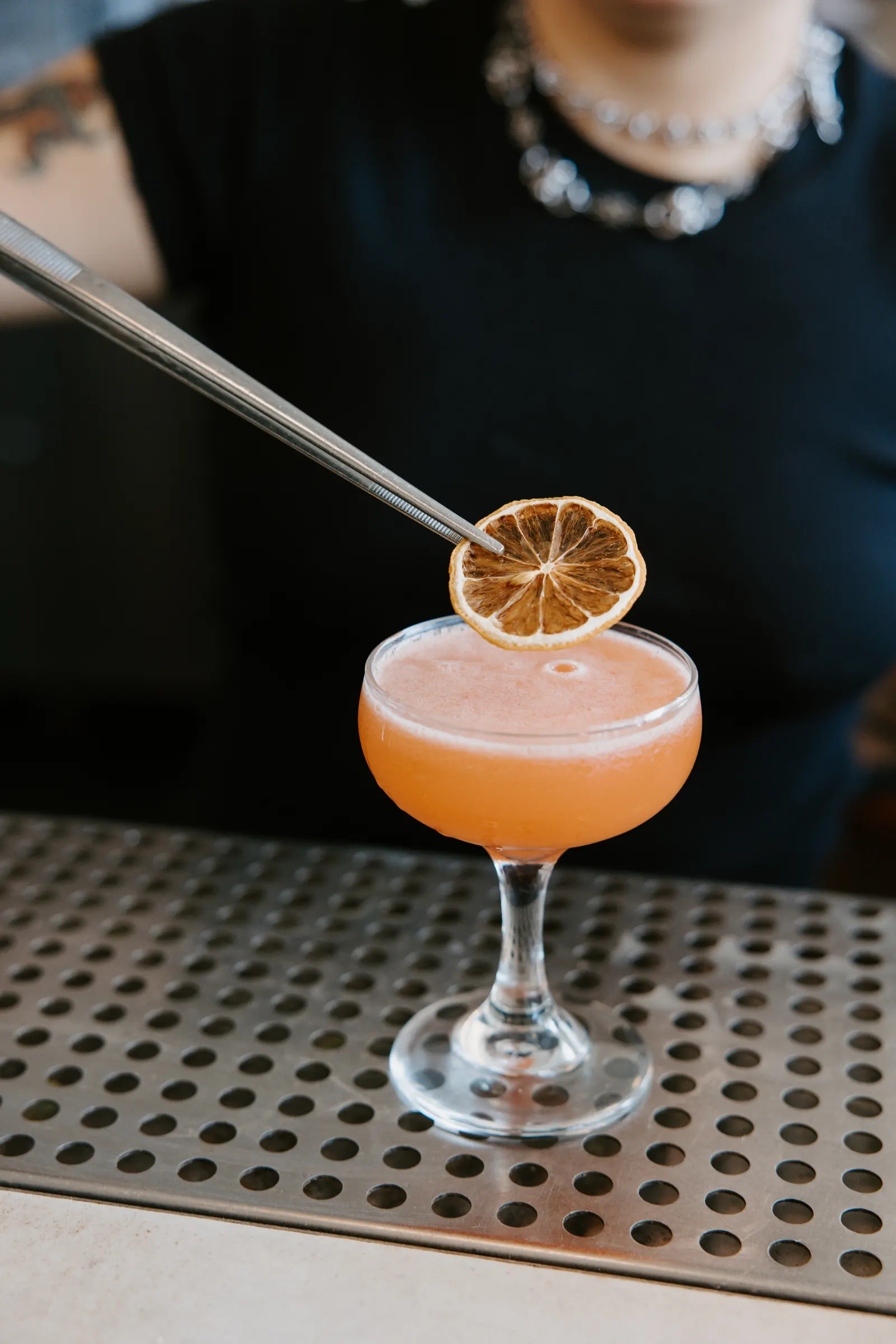 Bartender placing a dehydrated orange garnish on a coupe cocktail in natural light at Intermezzo