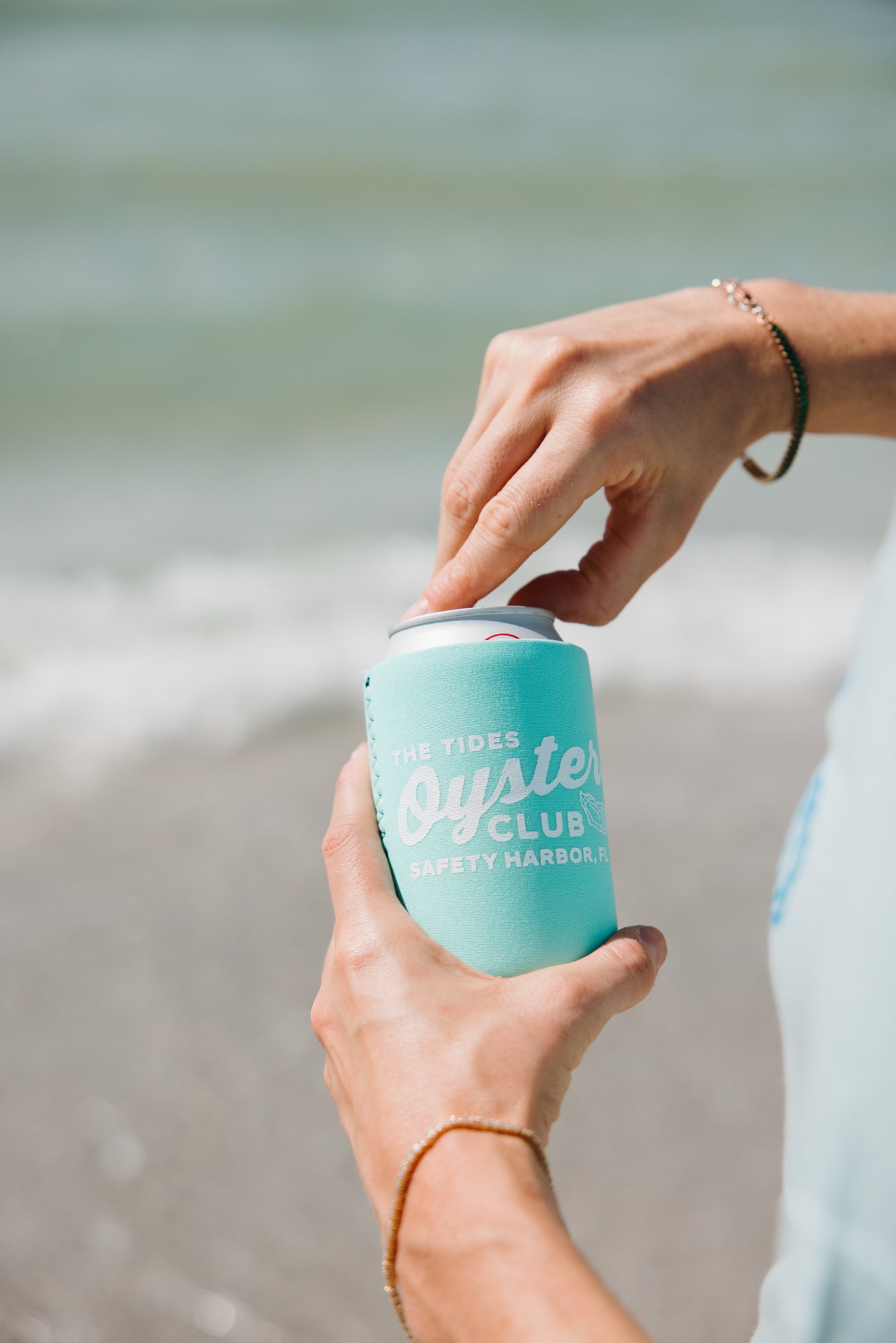 Branded koozie held against the ocean — in-the-wild product photography by Orange Grove Social