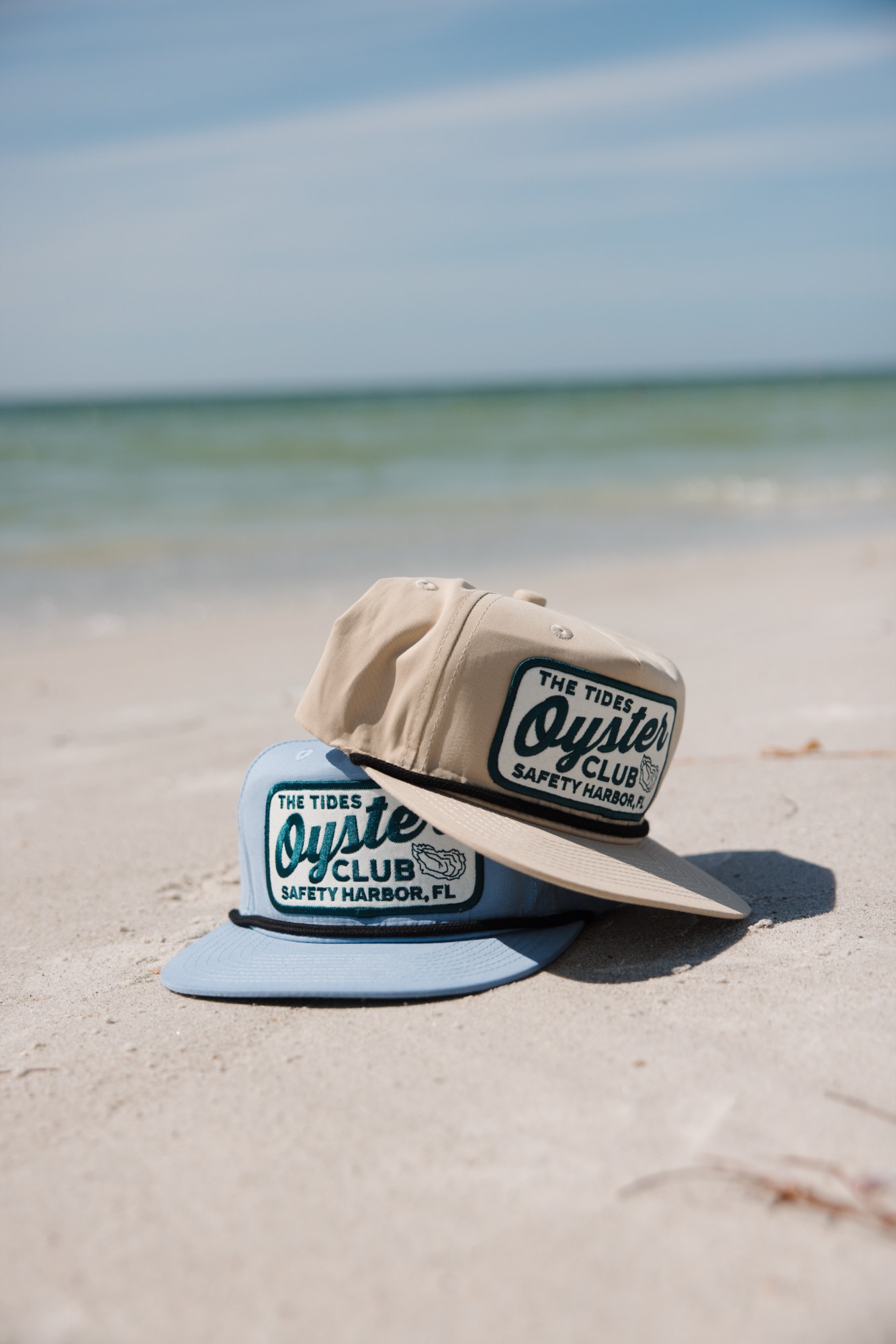 Branded hats styled in the sand — lifestyle product photography by Orange Grove Social