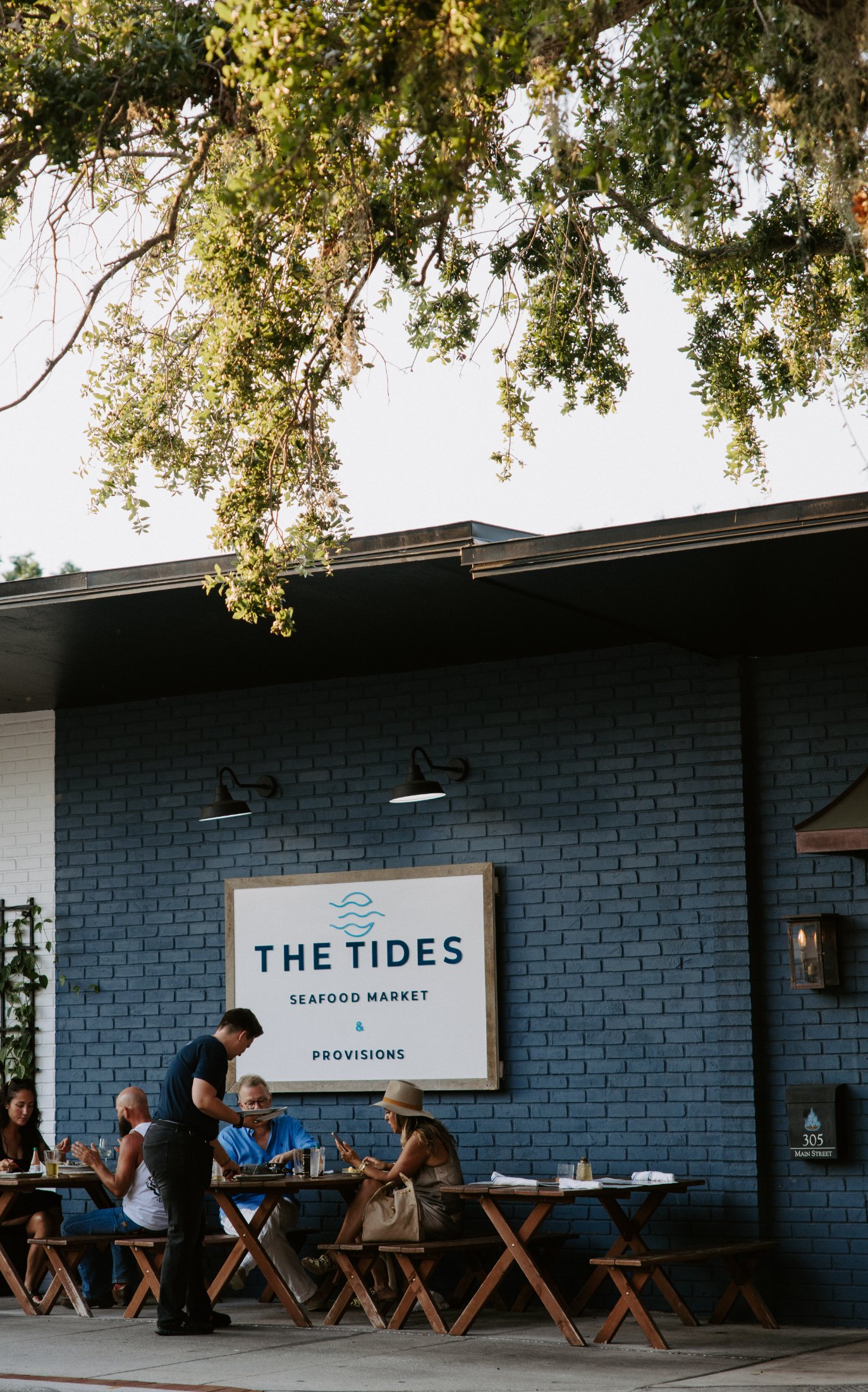 Guests dining on the patio beneath The Tides Seafood Market & Provisions sign in Safety Harbor FL